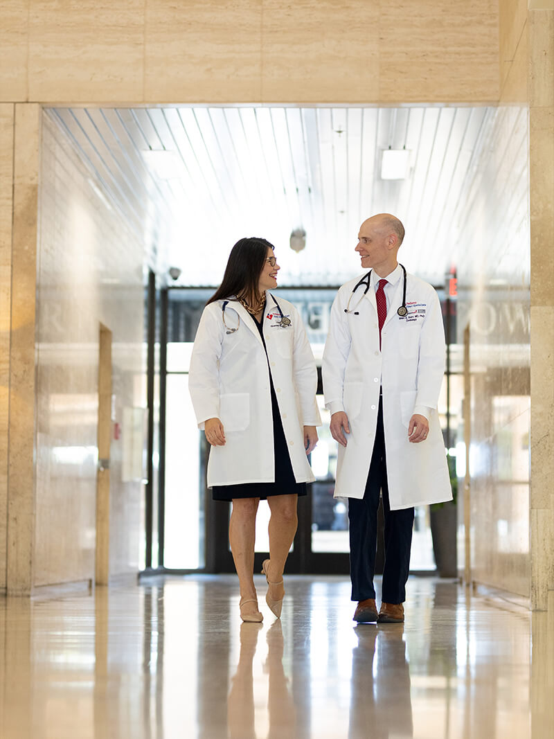 Drs walking down the hall of a hospital. One male, one female.